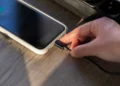 Mão conectando carregador em smartphone sobre mesa de madeira, representando um hábito comum de recarga que pode afetar a vida útil da bateria.