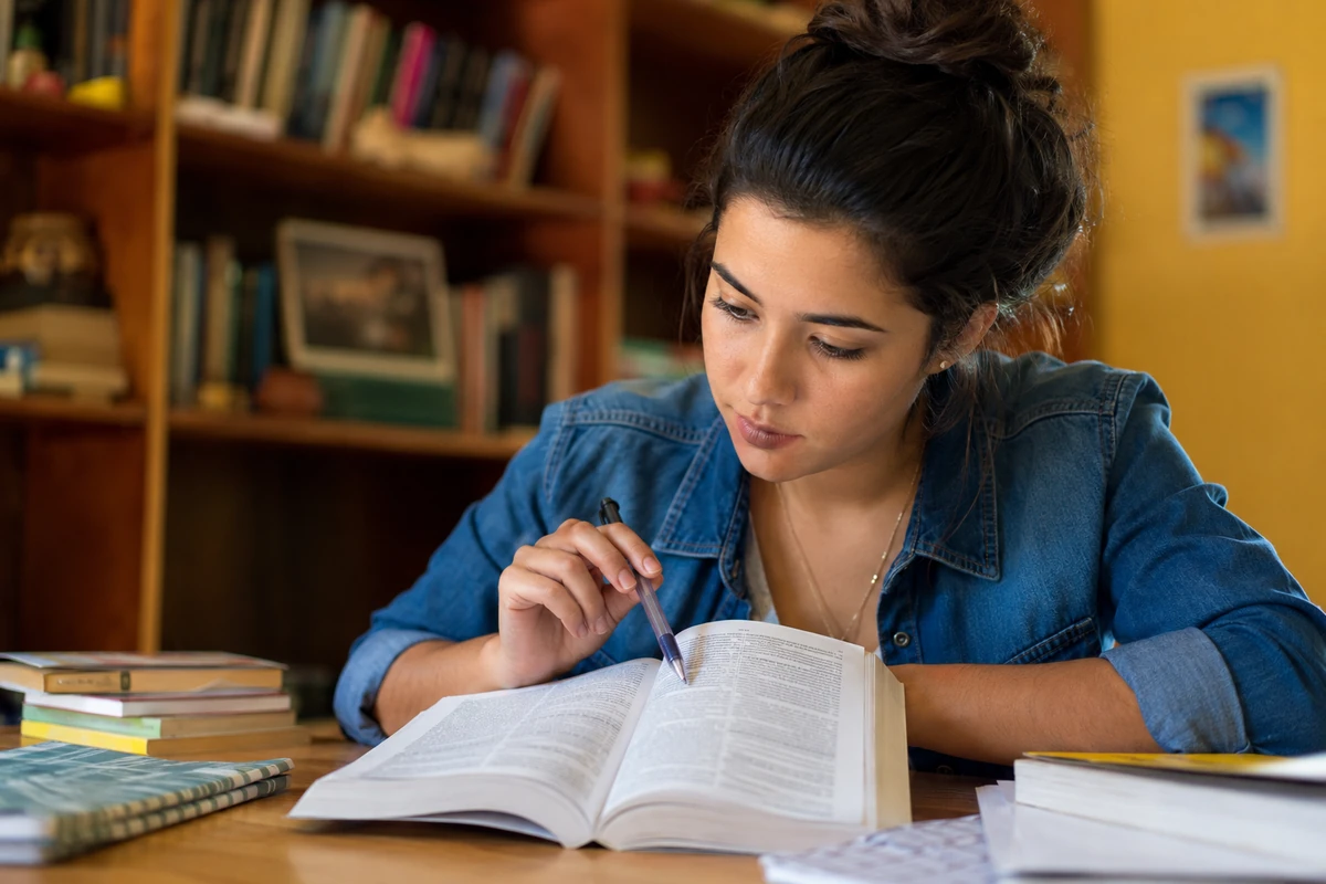 Estudante consultando um livro aberto para entender como aplicar “que” e “quê” corretamente nas frases.