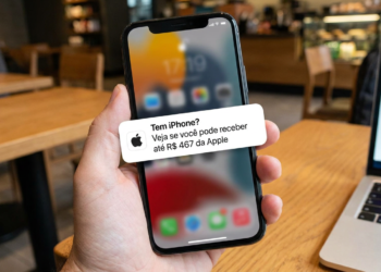 Mão segura iPhone exibindo notificação sobre indenização de R$ 467 da Apple em cafeteria.