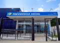 Fachada de uma agência da Previdência Social com grade na entrada e céu azul ao fundo.