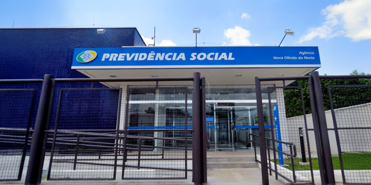 Fachada de uma agência da Previdência Social com grade na entrada e céu azul ao fundo.