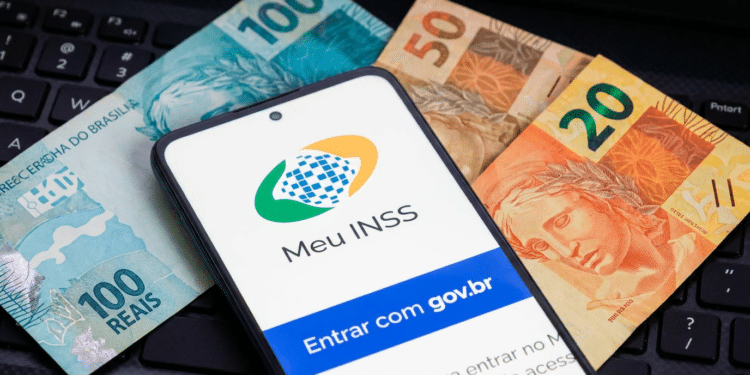 Smartphone exibindo tela do Meu INSS com botão gov.br sobre notas de 100, 50 e 20 reais em teclado preto.
