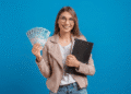 Mulher sorridente exibe notas de 100 reais com pasta em fundo azul.