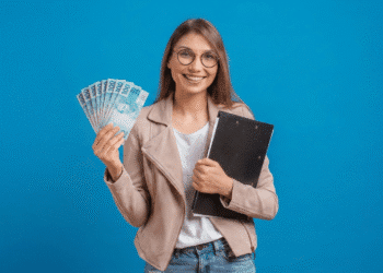 Mulher sorridente exibe notas de 100 reais com pasta em fundo azul.