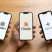 Três smartphones exibindo logos de ChatGPT, Claude e Gemini segurados por mãos sobre mesa de madeira.