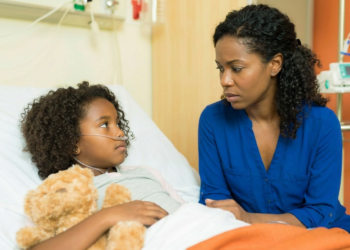 Mãe sentada ao lado da filha doente no hospital.