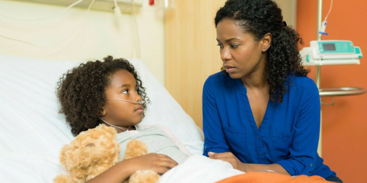 Mãe sentada ao lado da filha doente no hospital.