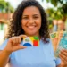 Mulher segurando cartão do Bolsa Família e notas de dinheiro, representando pagamento de junho.