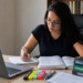 Mulher de óculos estuda com livros de Direito e bandeira do Brasil ao lado do notebook.