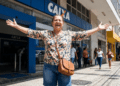 Mulher sorridente celebra em frente à agência Caixa Econômica Federal.
