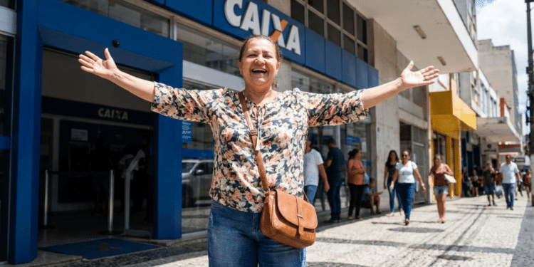 Mulher sorridente celebra em frente à agência Caixa Econômica Federal.