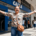 Mulher sorridente celebra em frente à agência Caixa Econômica Federal.