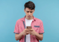 Jovem confuso olhando celular com expressão preocupada.