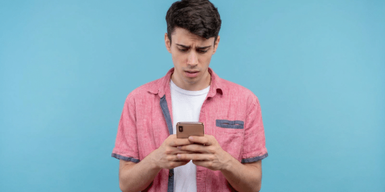 Jovem confuso olhando celular com expressão preocupada.