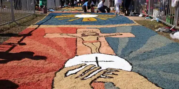 Tapete colorido de Corpus Christi com símbolos religiosos sendo confeccionado por participantes em procissão.