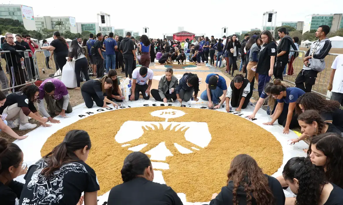 Tapete decorativo de Corpus Christi com pessoas confeccionando símbolos religiosos no chão.