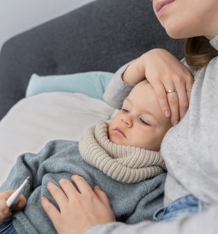 Mãe conforta filho doente deitado segurando termômetro.