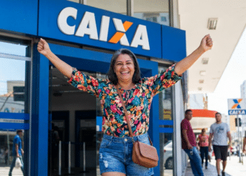 Mulher sorridente celebra conquista em frente à agência da Caixa.