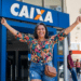 Mulher sorridente celebra conquista em frente à agência da Caixa.