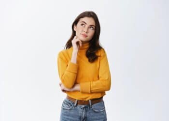 Jovem mulher pensativa de suéter amarelo em fundo branco.