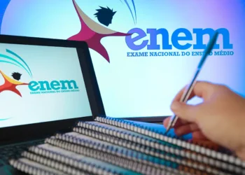 Notebook exibindo logo do Enem, cadernos empilhados e mão segurando caneta em fundo azul com marca do exame