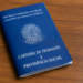 Carteira de Trabalho e Previdência Social azul fechada sobre superfície de madeira.