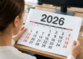 Mulher consulta calendário de 2026 em escritório organizado.