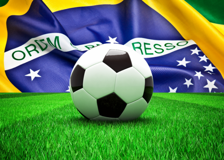 Jogos do Brasil na Copa do Mundo 2026. Bola de futebol em destaque no gramado com bandeira do Brasil ao fundo.