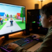Adolescente usando computador com tela mostrando Roblox, teclado colorido e ambiente iluminado.