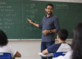 Professor explicando fórmula de Bhaskara no quadro verde, alunos atentos em sala de aula.