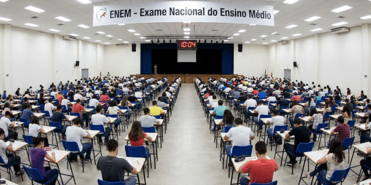 Centenas de estudantes fazem o Exame Nacional do Ensino Médio sentados em fileiras num auditório amplo.