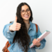 Jovem estudante sorridente com óculos faz sinal de positivo em fundo claro.