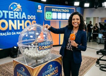 Mulher sorridente ao vivo mostra bola número 17 no sorteio da Loteria dos Sonhos, cenário azul