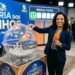 Mulher sorridente ao vivo mostra bola número 17 no sorteio da Loteria dos Sonhos, cenário azul