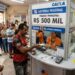 Pessoas em fila aguardam atendimento em lotérica com placa do prêmio de R$ 500 mil