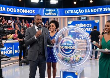 Apresentador anuncia sorteio da Loteria dos Sonhos com urna de bolas e plateia animada ao fundo.
