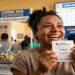 Mulher sorridente segura bilhete ganhador da Loteria dos Sonhos número 31947 em casa lotérica do Ceará