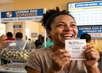 Mulher sorridente segura bilhete ganhador da Loteria dos Sonhos número 31947 em casa lotérica do Ceará