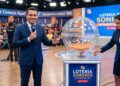 Apresentador sorri ao lado de globo de bolinhas e assistente exibe bola da Loteria dos Sonhos