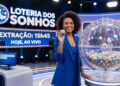 Apresentadora sorridente em estúdio segura bola 27 durante sorteio da Loteria dos Sonhos