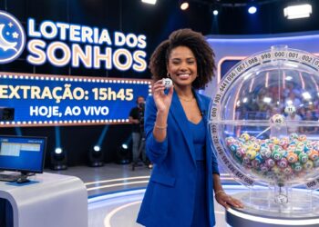 Apresentadora sorridente em estúdio segura bola 27 durante sorteio da Loteria dos Sonhos