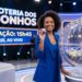 Apresentadora sorridente em estúdio segura bola 27 durante sorteio da Loteria dos Sonhos
