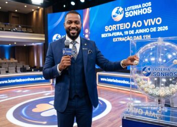 Homem sorrindo segura microfone ao lado de globo de bolinhas da Loteria dos Sonhos no estúdio