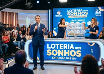 Apresentador anuncia sorteio da Loteria dos Sonhos com duas assistentes e público ao fundo em estúdio iluminado