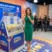 Mulher vestindo verde anuncia bolinha na Loteria dos Sonhos com auditório ao fundo