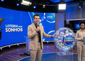 Apresentador e funcionária exibem globo com bolas e número 14 no sorteio da Loteria dos Sonhos