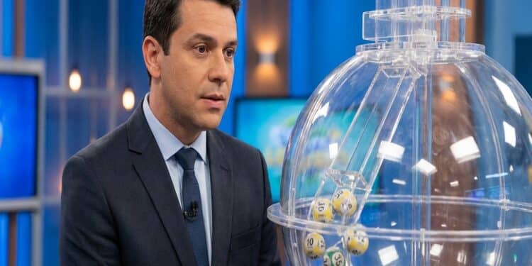 Apresentador de terno azul-marinho ao lado de globo de sorteio com bolas numeradas em estúdio de TV