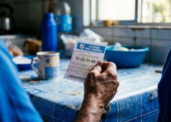 Pessoa idosa confere bilhete da Loteria dos Sonhos com números à mesa azul