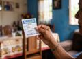 Mulher segurando bilhete da Loteria dos Sonhos Ceará em sala de casa decorada com fotos