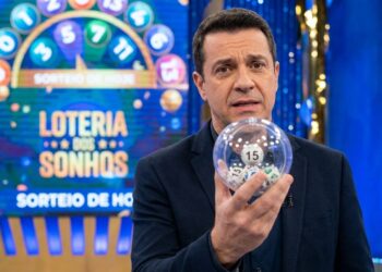 Homem de terno segura globo transparente com bola número 15 em estúdio da Loteria dos Sonhos